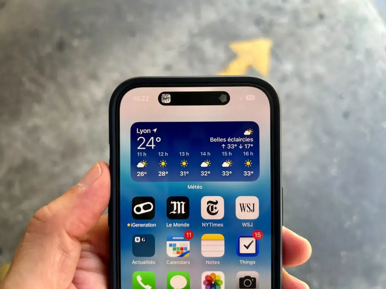 iPhone avec la Dynamic Island affichant la météo à Lyon. La barre d'état montre l'heure et le niveau de batterie.
