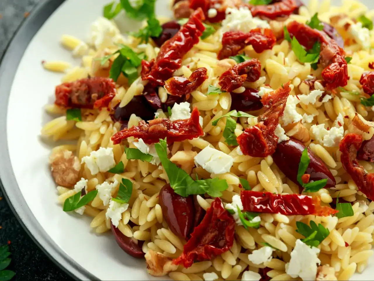 Pyszna sałatka z makaronu orzo, suszonych pomidorów, oliwek, sera feta i świeżej bazylii.