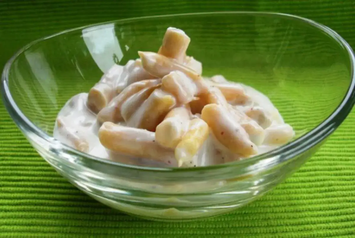Gelber Bohnensalat in einer Glasschüssel auf grünem Hintergrund.