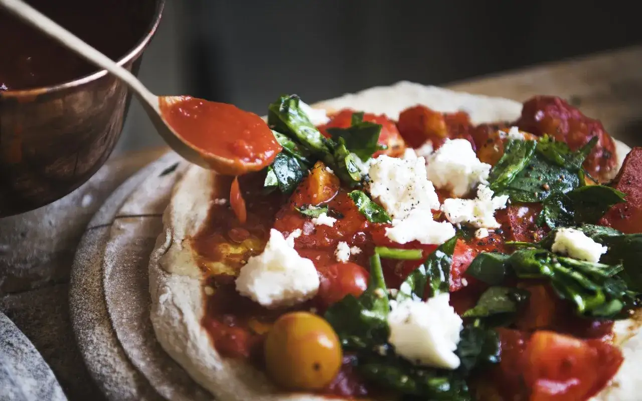 Sos pomidorowy dodawany łyżką do pizzy z serem i bazylią.