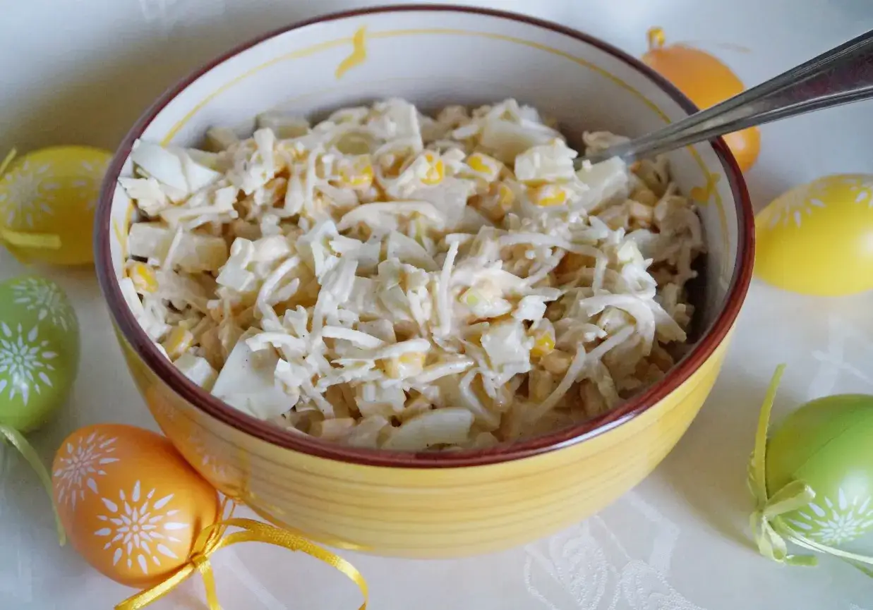 Pyszna sałatka z ananasem, jajkiem i kukurydzą w żółtej misce, otoczona kolorowymi pisankami. Idealna na Wielkanoc!