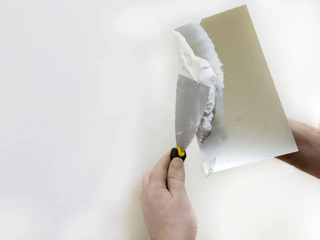 Dłoń z kielnią nakłada masę na ścianę. Kluczowe jest odpowiednie jaki grunt pod gładź polimerowa, by uzyskać idealnie gładką powierzchnię.