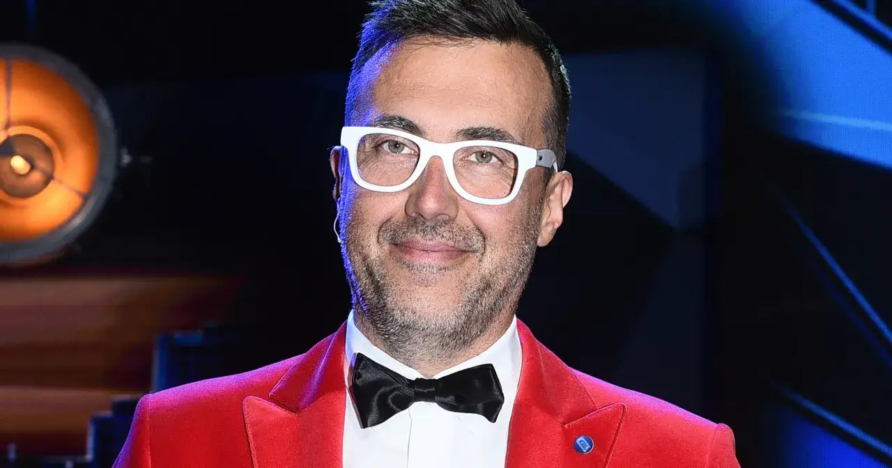 DJ Adamus w czerwonej marynarce i białych okularach, z czarną muszką.