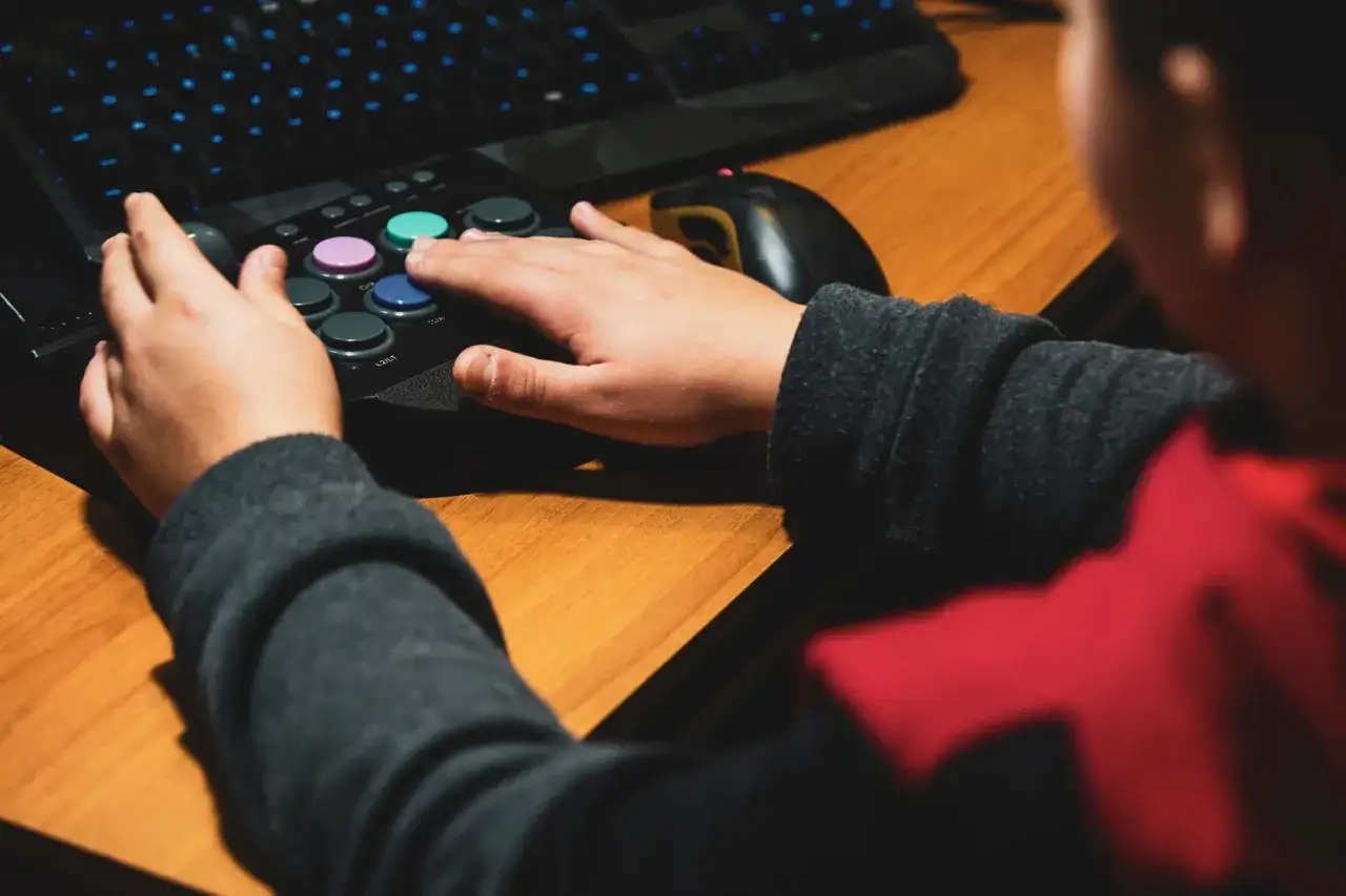 Dłonie gracza na joysticku i klawiaturze, obok myszka komputerowa.