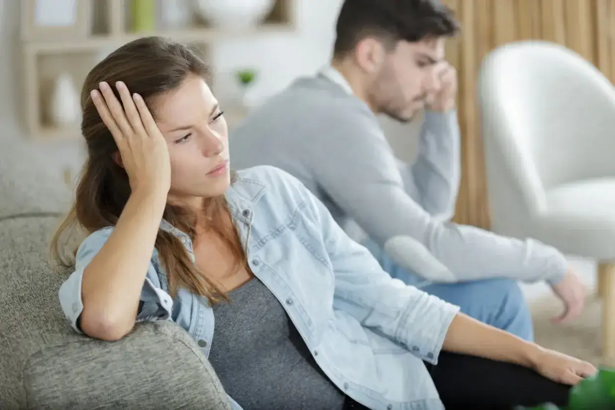 Para siedząca na kanapie, odwrócona od siebie, z wyrazem zmartwienia na twarzy.