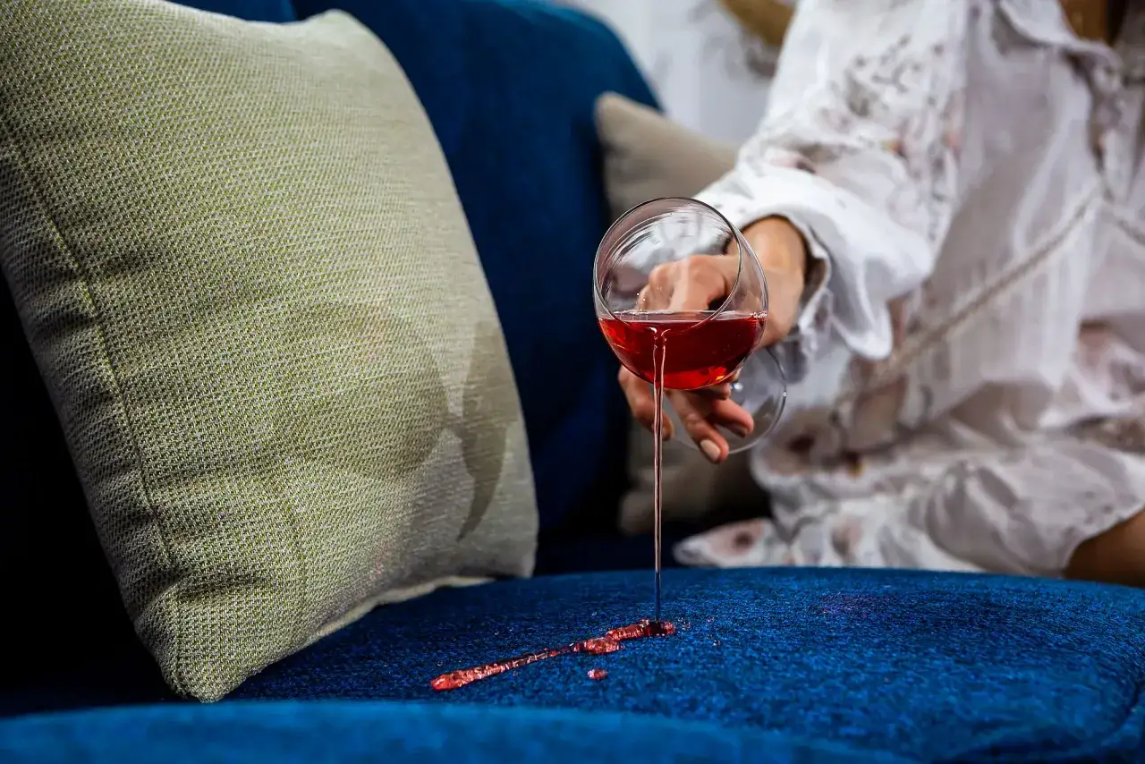 Wino rozlane na granatową kanapę. Jasna poduszka obok, a na niej plamy. Idealne tkaniny obiciowe łatwe do czyszczenia.