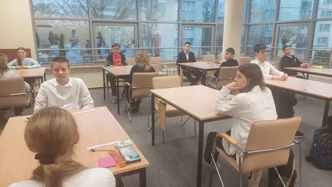 Uczniowie podczas mscdn konkursy przedmiotowe. Młodzi ludzie siedzą przy stołach, skupieni na zadaniach.
