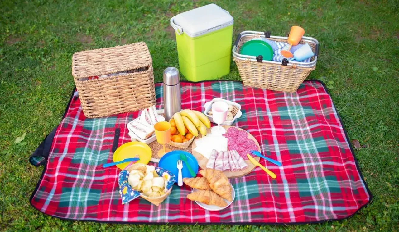 Co zabrac na piknik? Koszyk, lodówkę, koce, jedzenie: kanapki, owoce, wędliny, croissanty, napoje i naczynia.