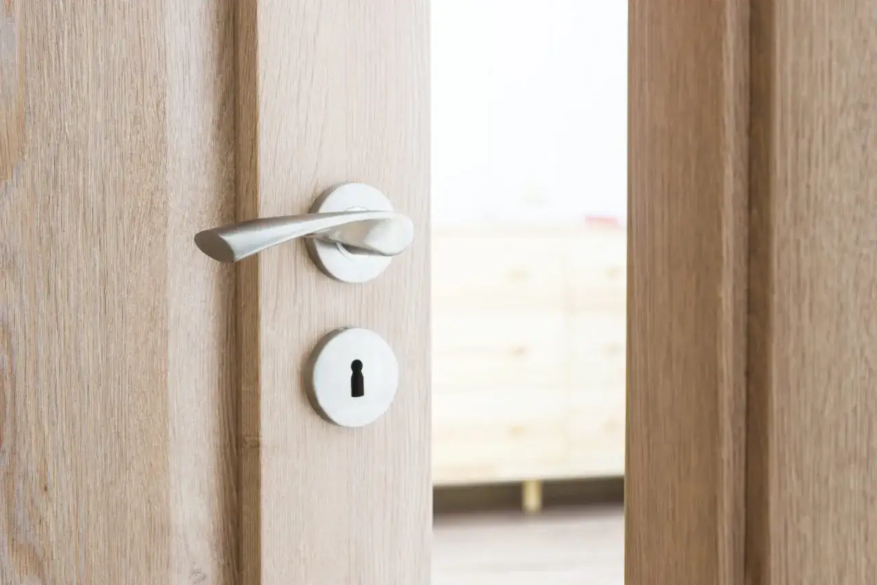 Drewniane drzwi z metalową klamką i otworem na klucz, uchylone.