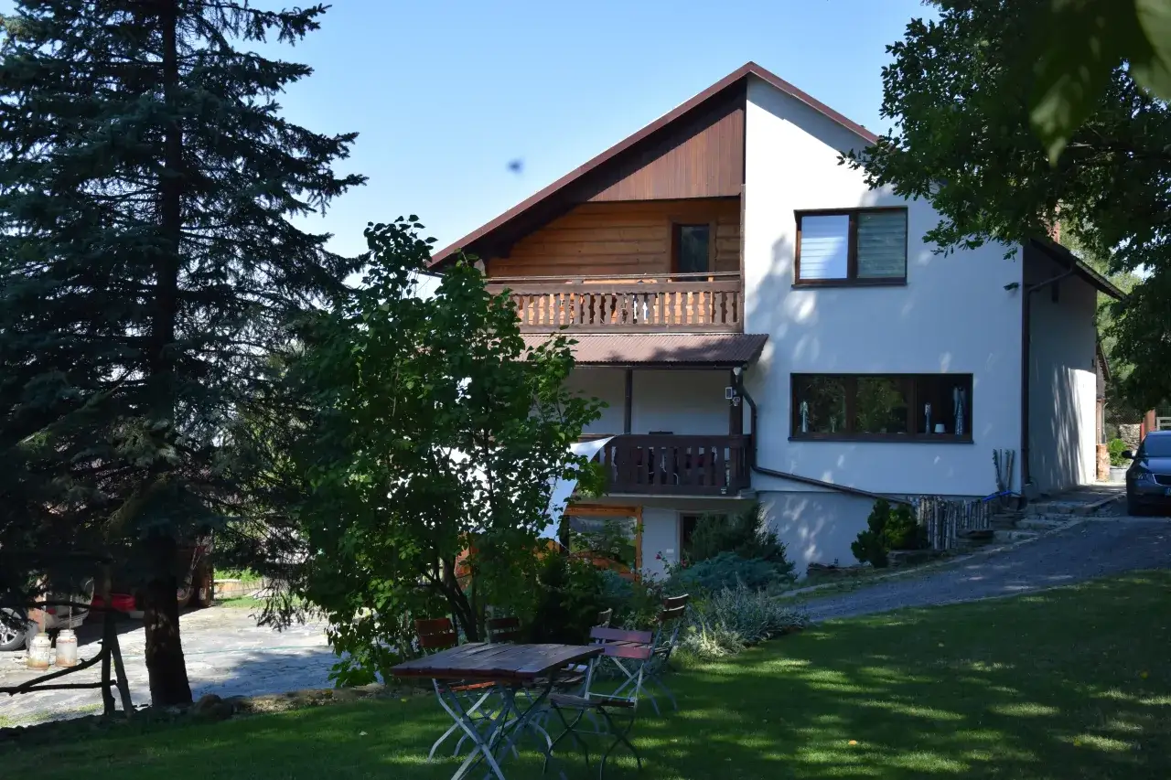 Agroturystyka Bacówka Giemzików zaprasza do wypoczynku. Dom z drewnianymi elementami i balkonami, otoczony zielenią, z miejscem do siedzenia na trawie.