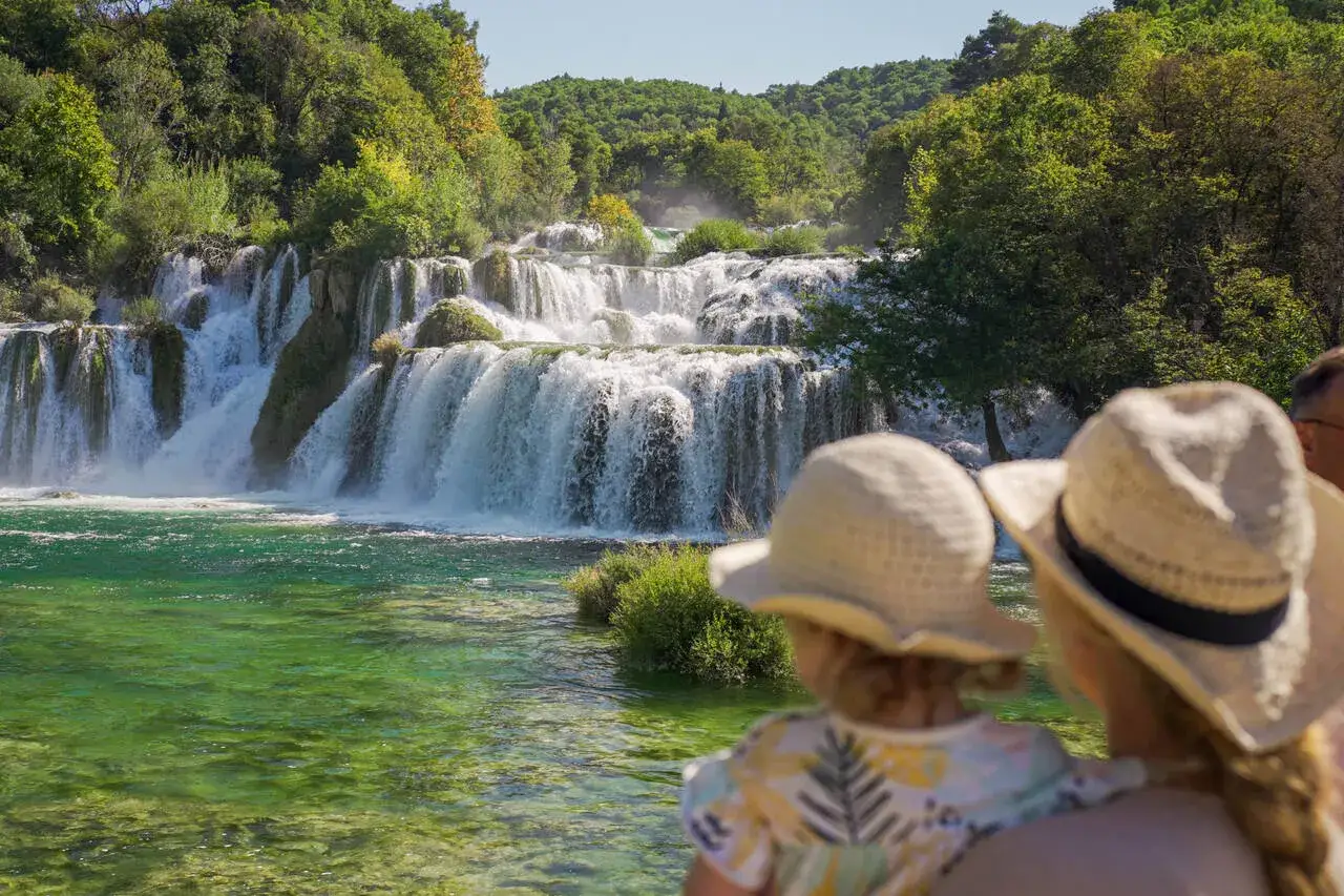 Rodzina podziwia malowniczy Roski slap. Woda spływa kaskadami po skałach, tworząc mgiełkę.