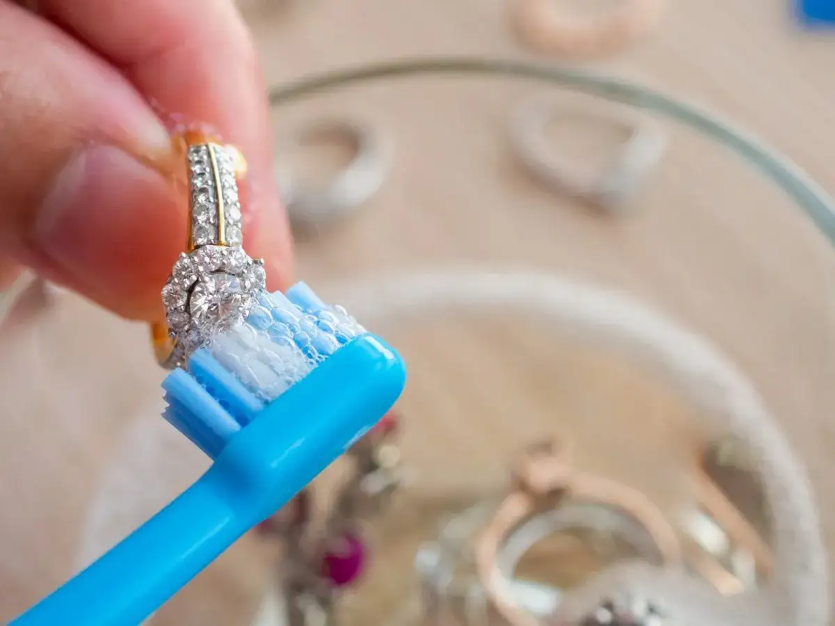 Dłoń czyści pierścionek z cyrkoniami niebieską szczoteczką z pianą.
