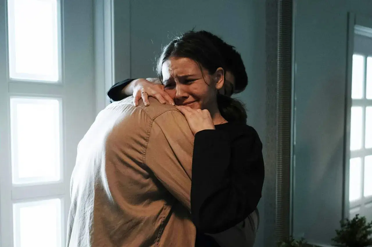 Kobieta płacze, przytulając się do ramienia innej osoby.