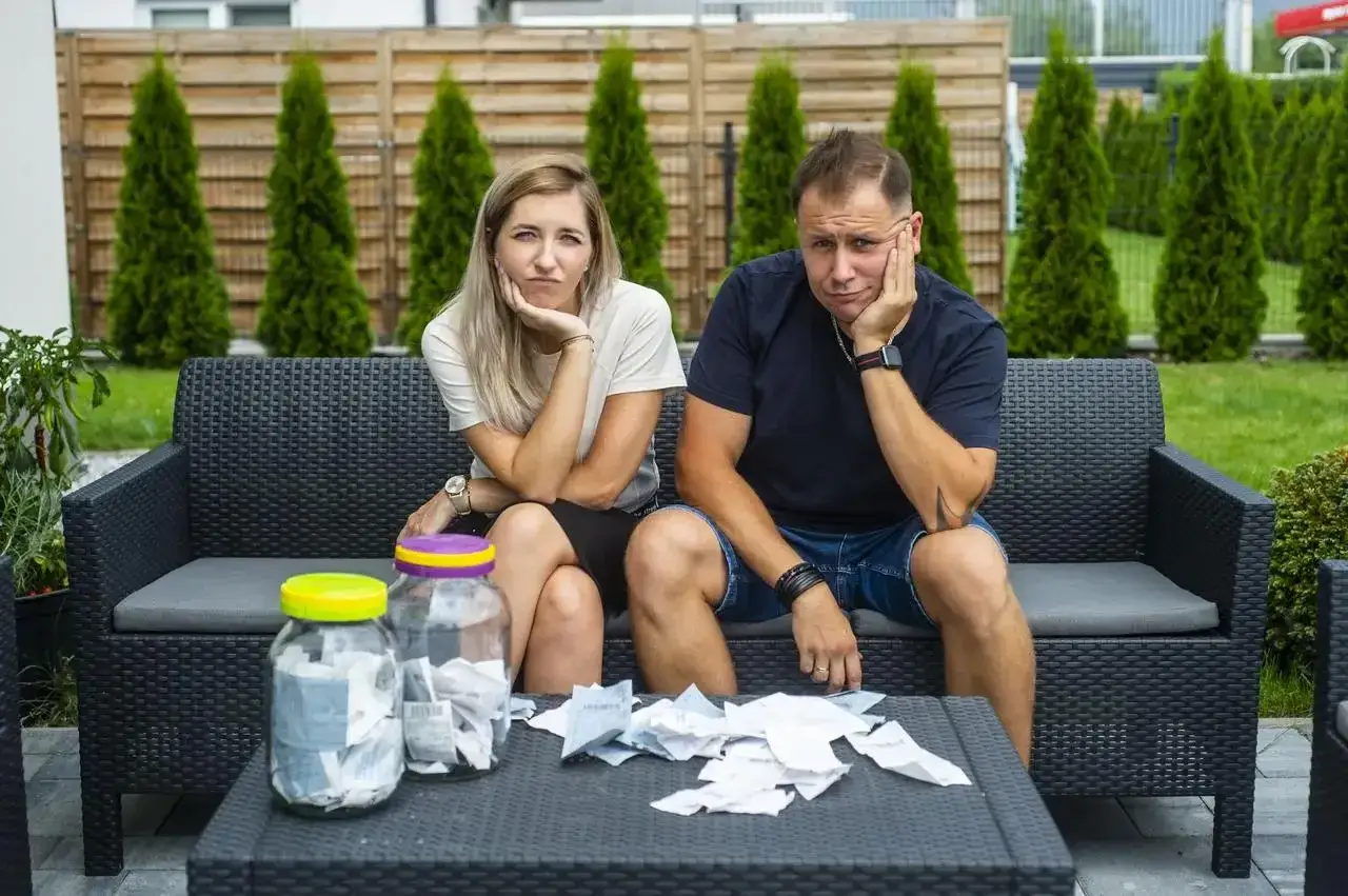 Zmartwieni uczestnicy programu "życie na kredycie" siedzą na kanapie, otoczeni rachunkami.