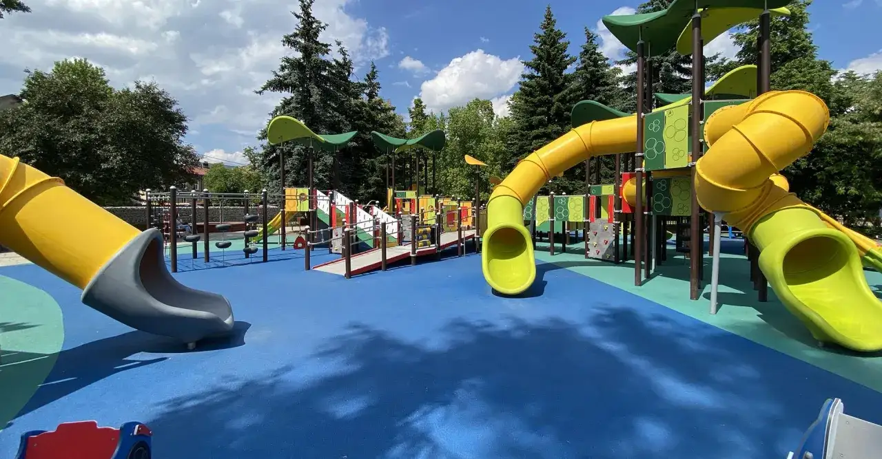 Kolorowy plac zabaw z żółtymi zjeżdżalniami i niebieską nawierzchnią.