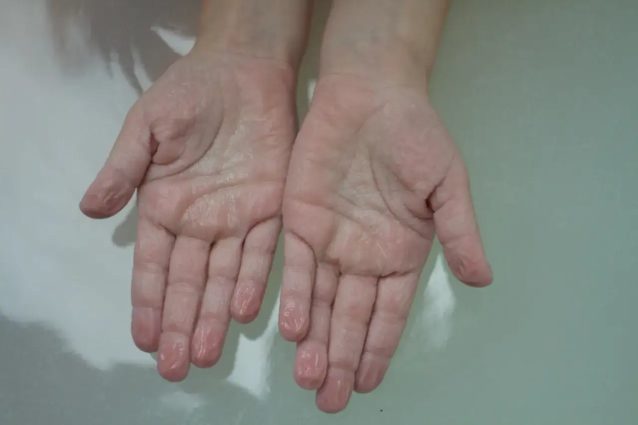 Młode dłonie, lekko pomarszczone po kąpieli, z kroplami wody na palcach.