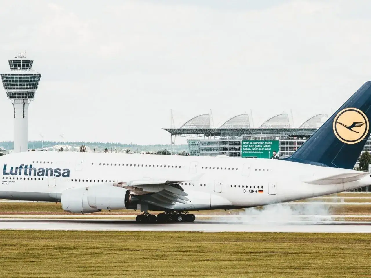 Lufthansa-Flugzeug landet auf dem Rollfeld, Rauch steigt auf.