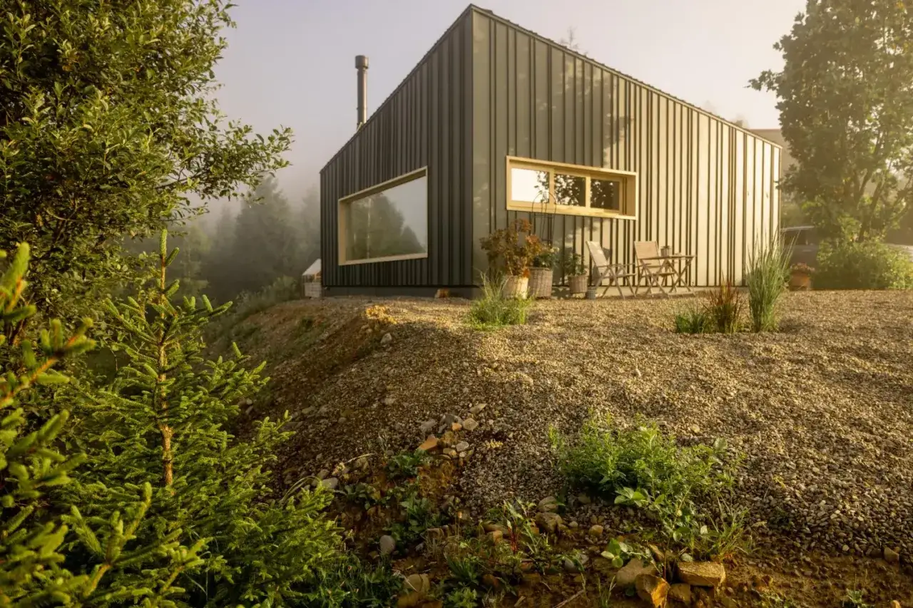 Nowoczesny dom z dużymi oknami na zboczu, otoczony zielenią. Rozpiętość konstrukcji jest imponująca, harmonijnie wkomponowana w krajobraz.