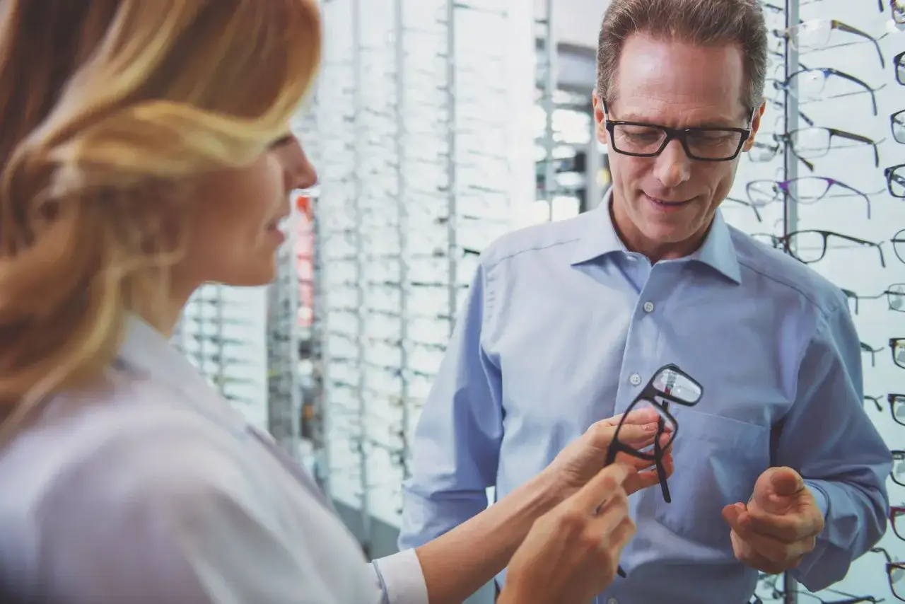 Kobieta w okularach pokazuje mężczyźnie okulary w salonie optycznym.