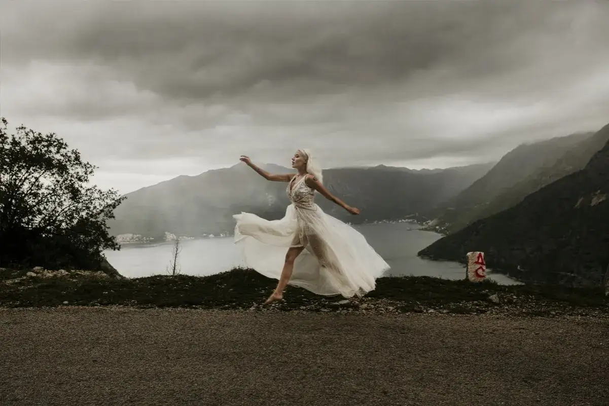 Panna młoda w zwiewnej sukni tańczy na tle gór i zatoki. Kiedy najlepiej kupić suknię ślubną?
