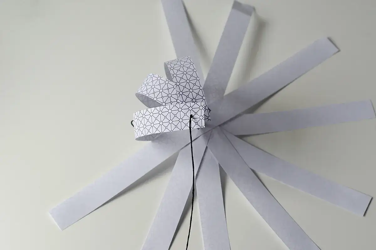 Papierowa ozdoba choinkowa 3D w trakcie tworzenia, z pasków z geometrycznym wzorem.