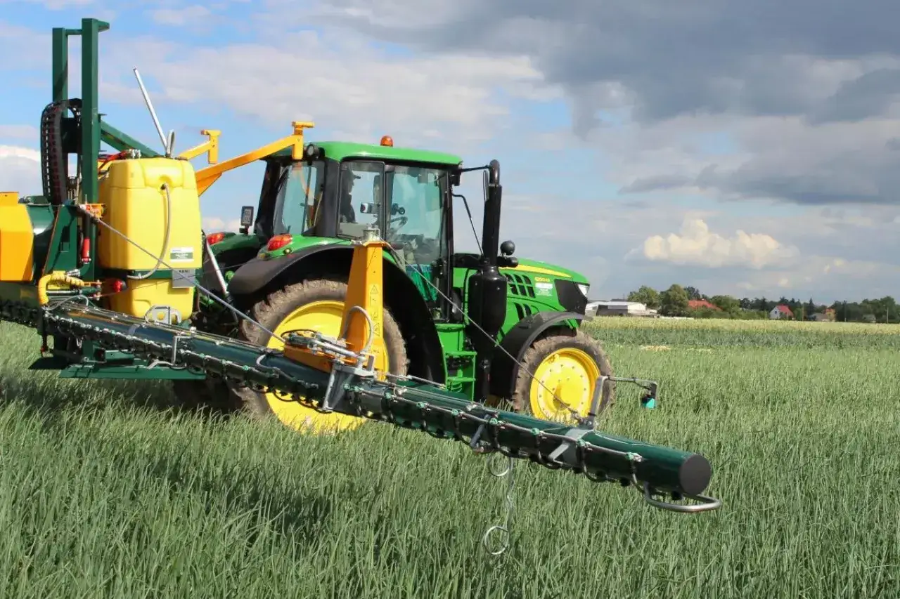 Zielony traktor z opryskiwaczem na polu. Warto sprawdzić movento 100 sc dawkowanie dla optymalnych rezultatów.