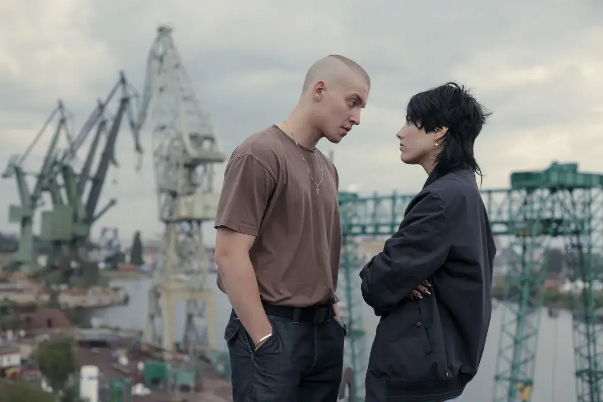 Para z napiętymi minami na tle stoczniowych dźwigów. On mówi: "Musimy ją odnaleźć, musimy ją **bring back Alice**".