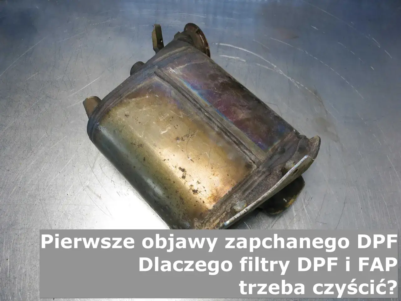 Brudny, metalowy filtr DPF leżący na szarej, metalowej powierzchni.