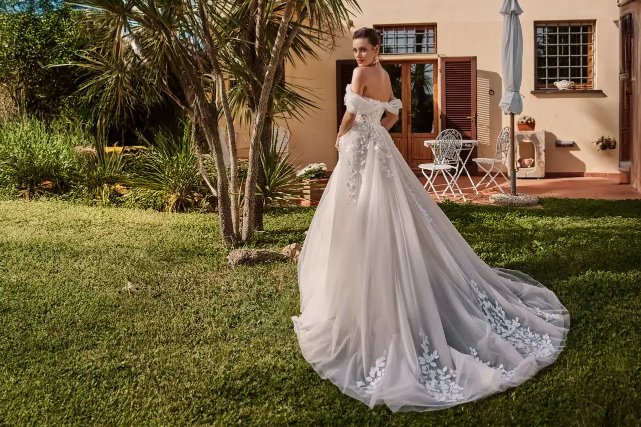 Panna młoda w sukni ślubnej z trenem na trawniku przed budynkiem.