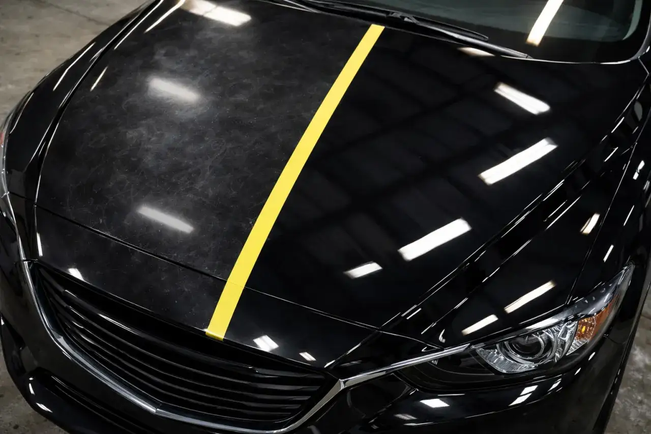 Czarne auto z żółtym pasem dzielącym matową, porysowaną maskę od błyszczącej, lustrzanej.