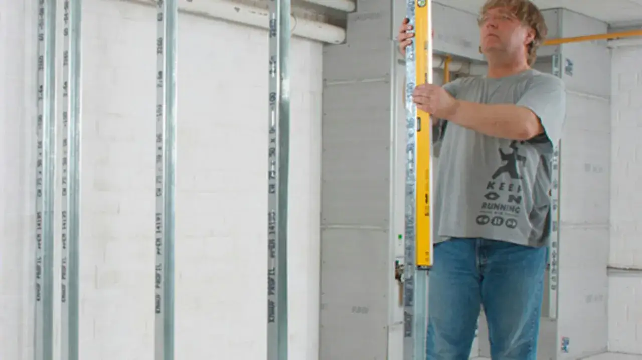 Mężczyzna z poziomicą sprawdza pionowe profile, przygotowując się do montażu półek z karton gipsu.