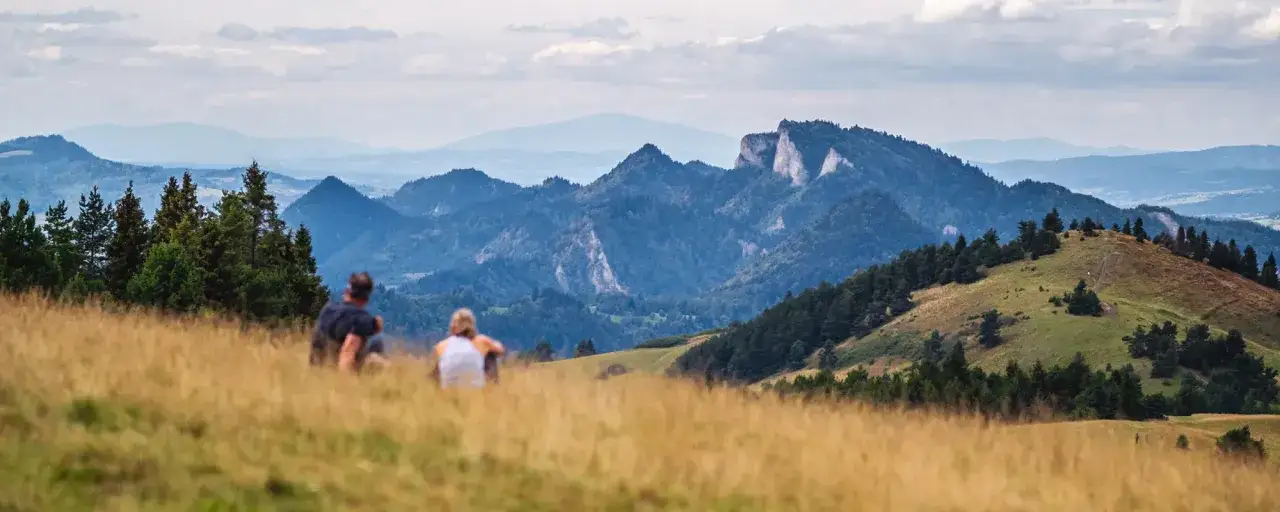 Para siedząca na trawiastym wzgórzu z widokiem na góry Pieniny.