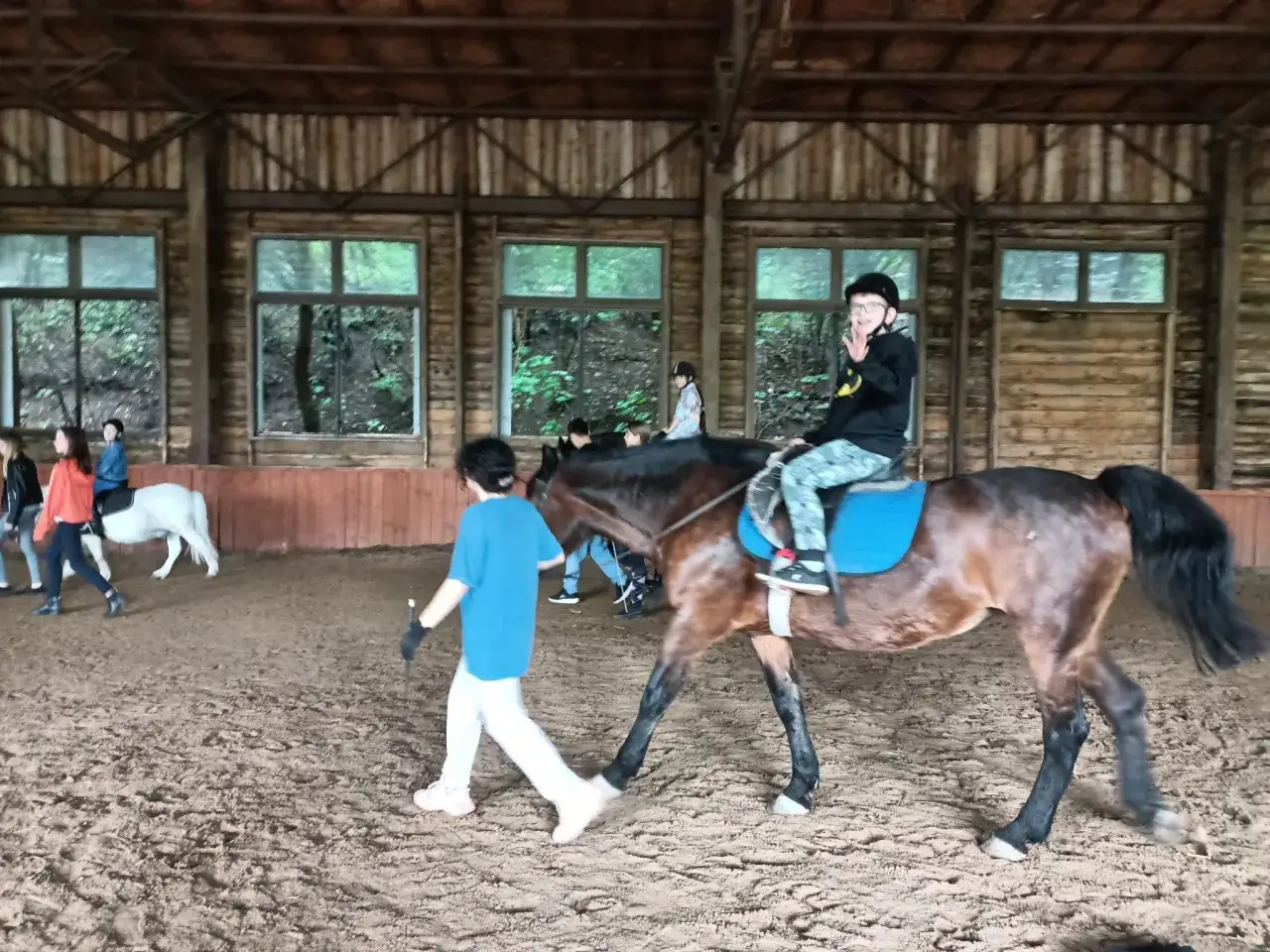 W stajni Black Horse Team Gdańsk, w owczarni, chłopiec na koniu macha do widza, a obok niego idzie instruktorka.