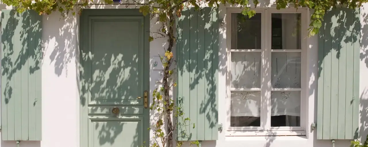 Zielony dom z okiennicami i drzwiami, ozdobiony winoroślą. Świetny pomysł na okiennice, które dodają uroku!