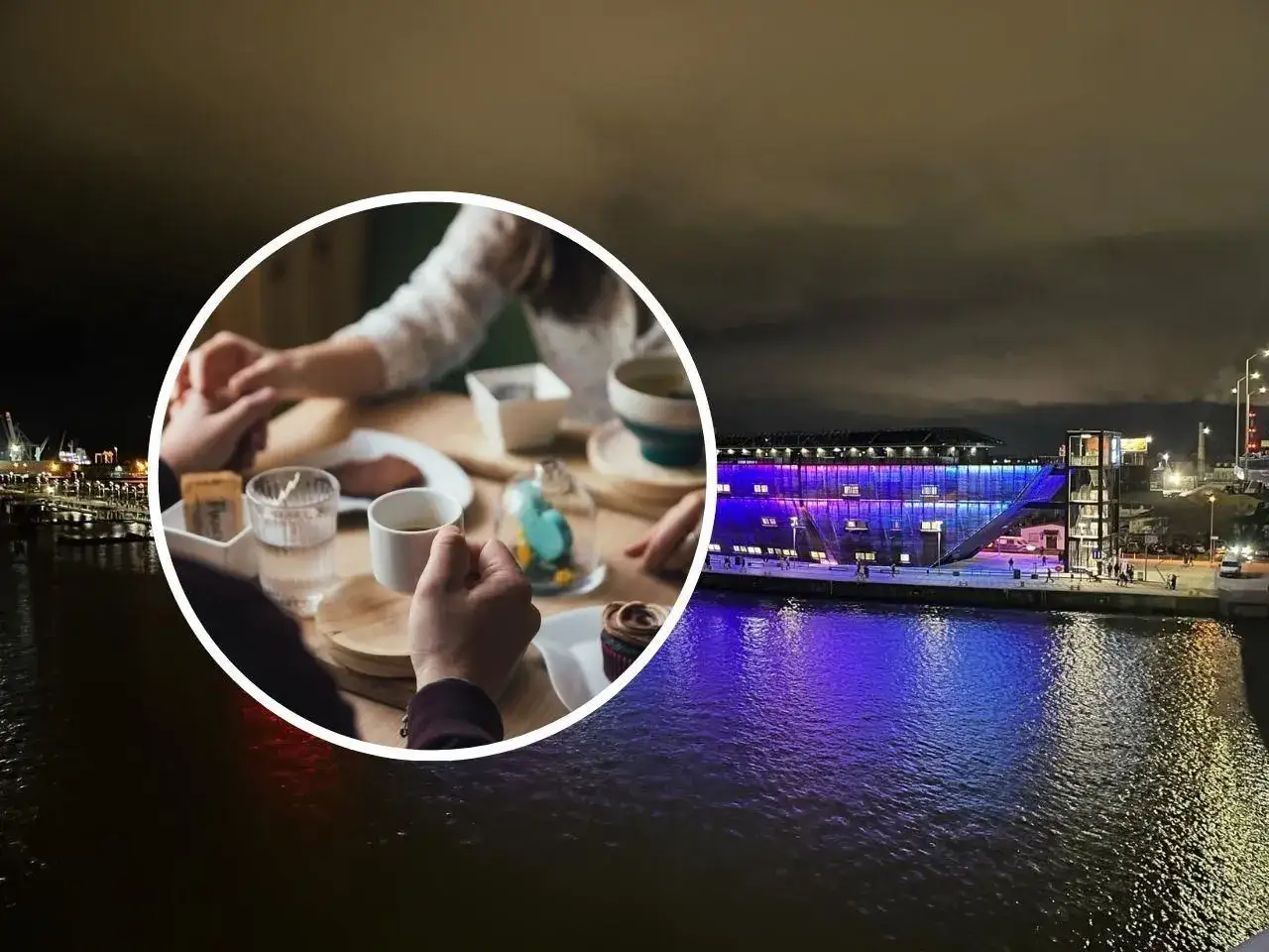 Para trzymająca się za ręce przy stoliku z kawą i ciastkiem, na tle nocnego Szczecina z oświetloną budowlą nad wodą.