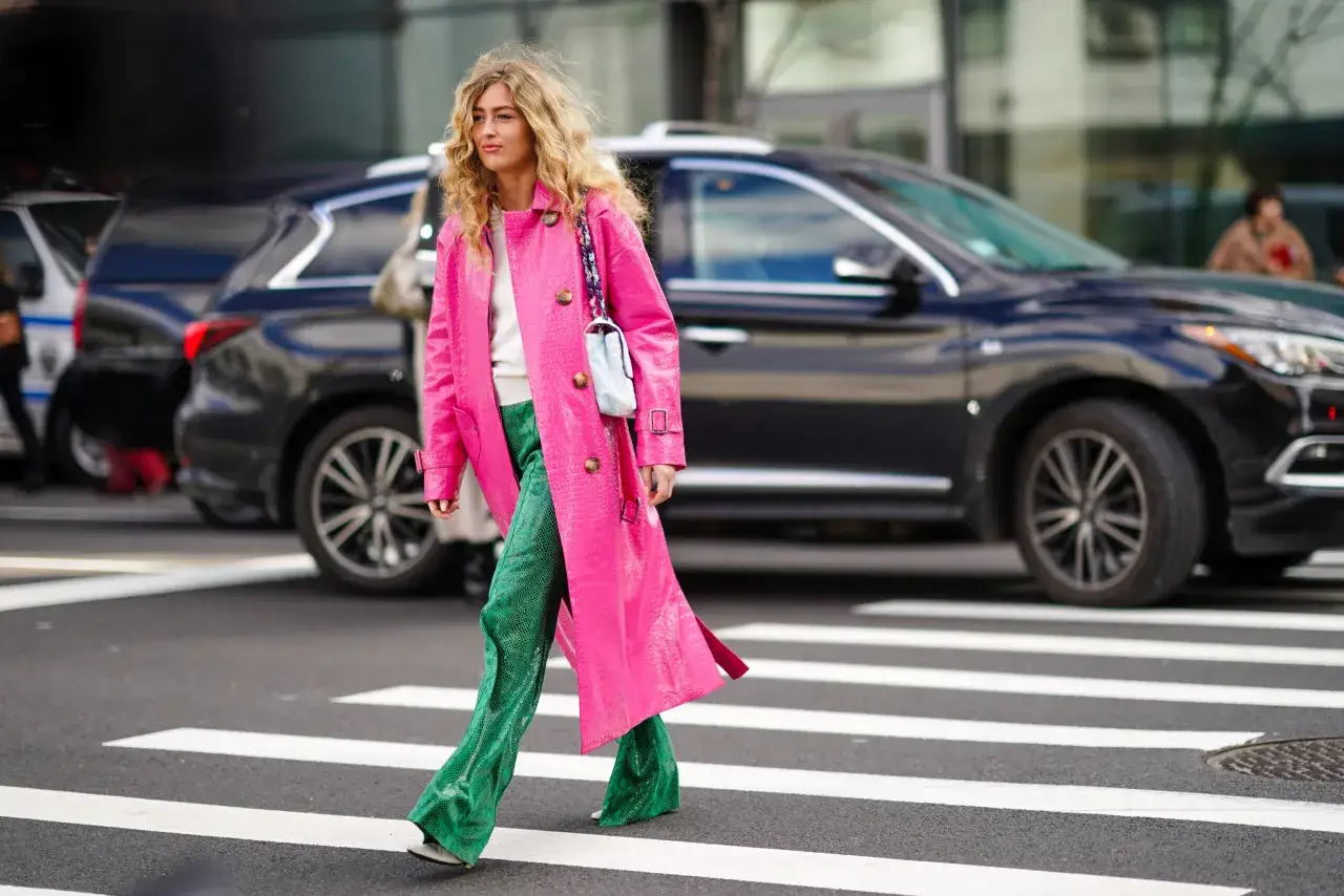 Kobieta w płaszczu w kolorze pudrowego różu i spodniach w butelkowej zieleni przechodzi przez pasy.