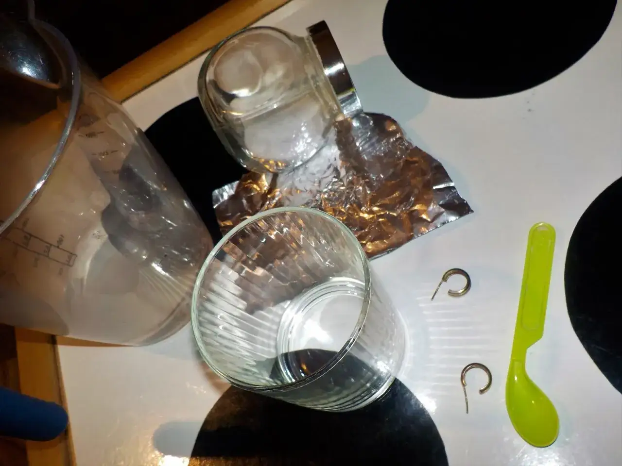 Szklanka, folia aluminiowa, sól, łyżeczka i kolczyki na blacie.