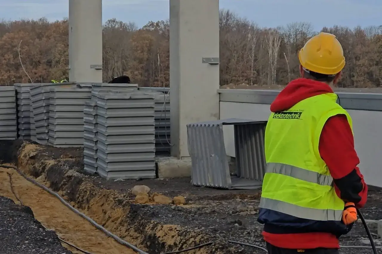 Pomocnik elektryka w kamizelce odblaskowej na budowie.