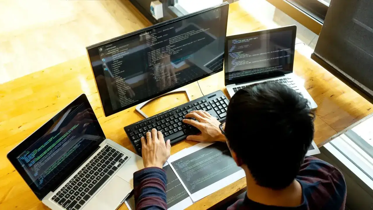 Programista pracuje przy biurku z trzema ekranami, pokazując, jak używać laptopa jako monitora.