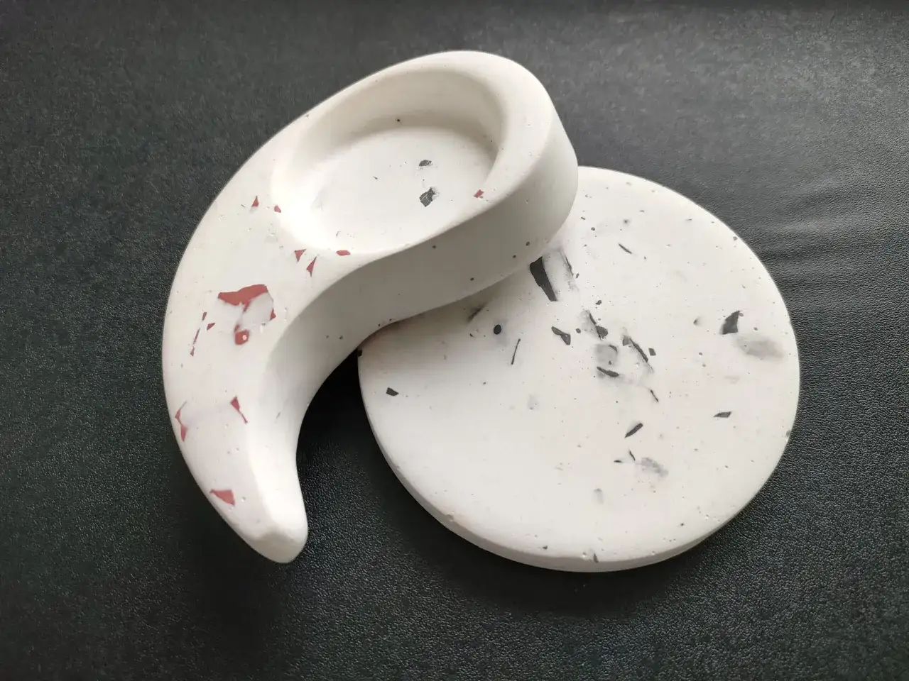 Gips polimerowy gdzie kupić? Dwa ozdobne elementy z gipsu polimerowego, jeden w kształcie półksiężyca, drugi okrągły, z czarnymi i czerwonymi wtrąceniami.