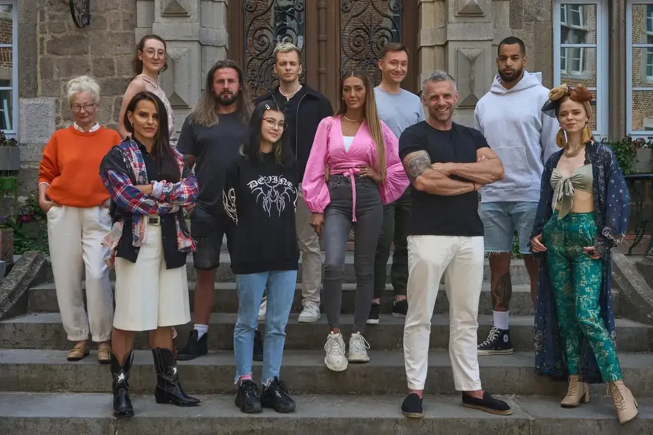 Grupa uczestników programu "The Traitors" pozuje na schodach.