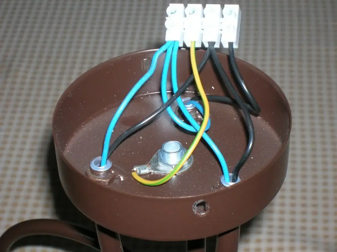 Podłączanie żyrandola: 3 kable z sufitu (niebieski, czarny, żółto-zielony) wchodzą do brązowej obudowy i są łączone w kostce.