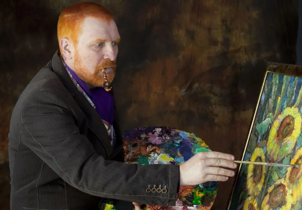 Mężczyzna z rudą brodą i fajką w ustach maluje słoneczniki, przypominając słynne van Gogh obrazy.