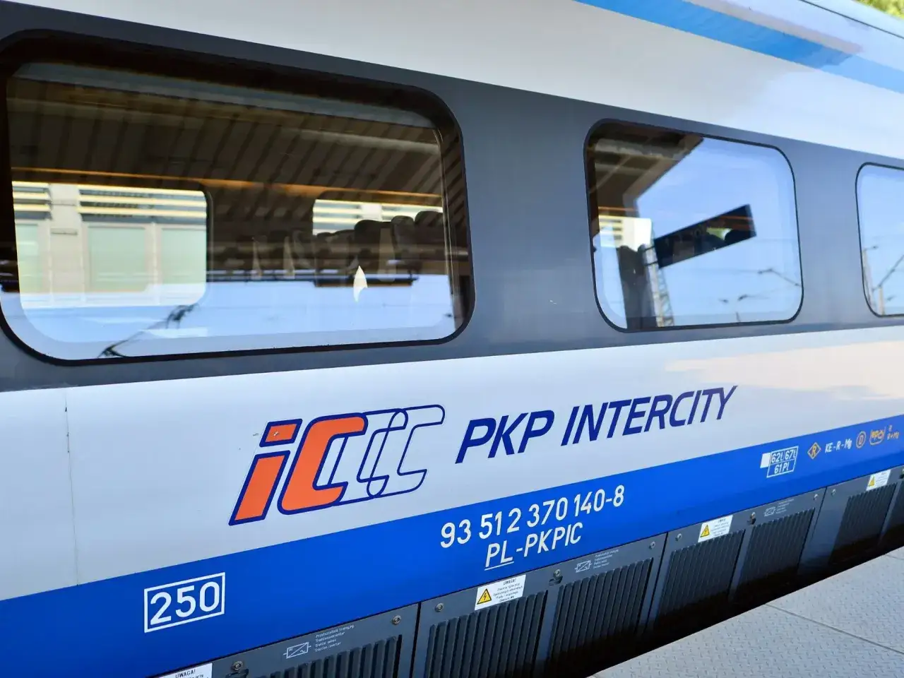 Boczna ściana pociągu PKP Intercity z logo IC. Widoczne okna, w których odbija się niebo i peron. To właśnie eic co to za pociąg!