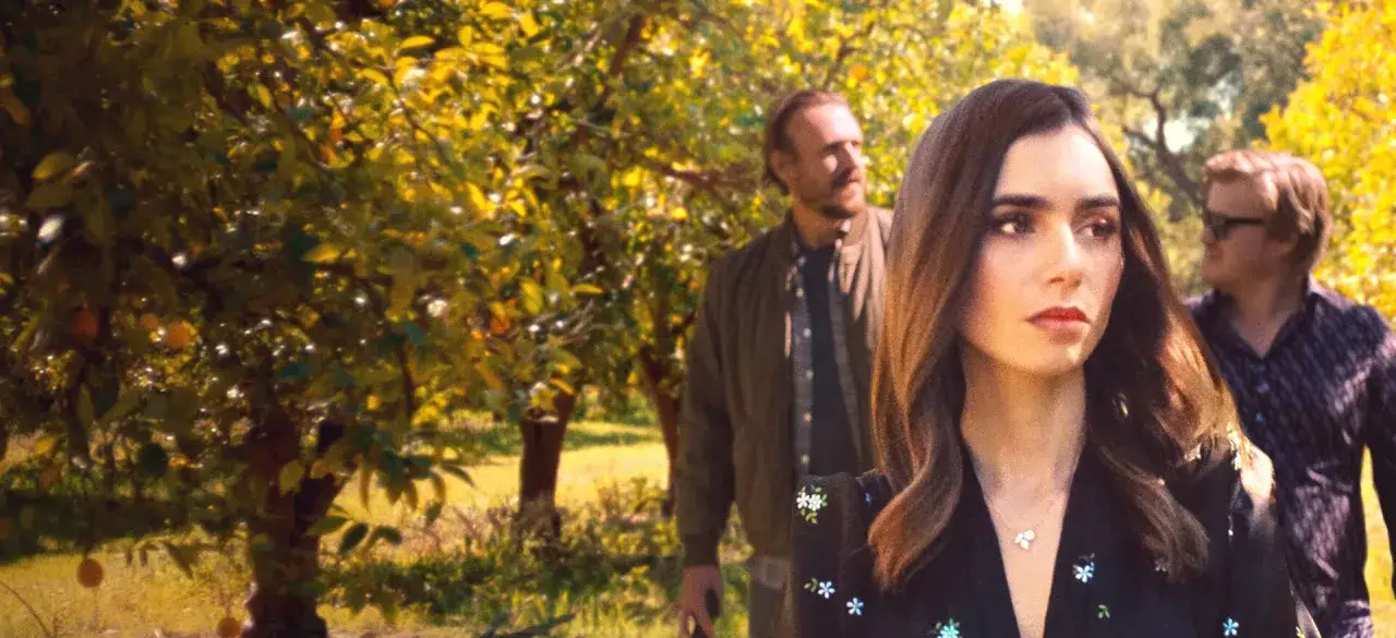 Kobieta z naszyjnikiem w kształcie serca idzie przez sad. Za nią dwaj mężczyźni. To jak prezent od losu.