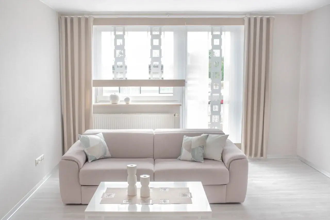 Jasny wystrój okna tarasowego z beżowymi zasłonami, sofą i stolikiem kawowym.