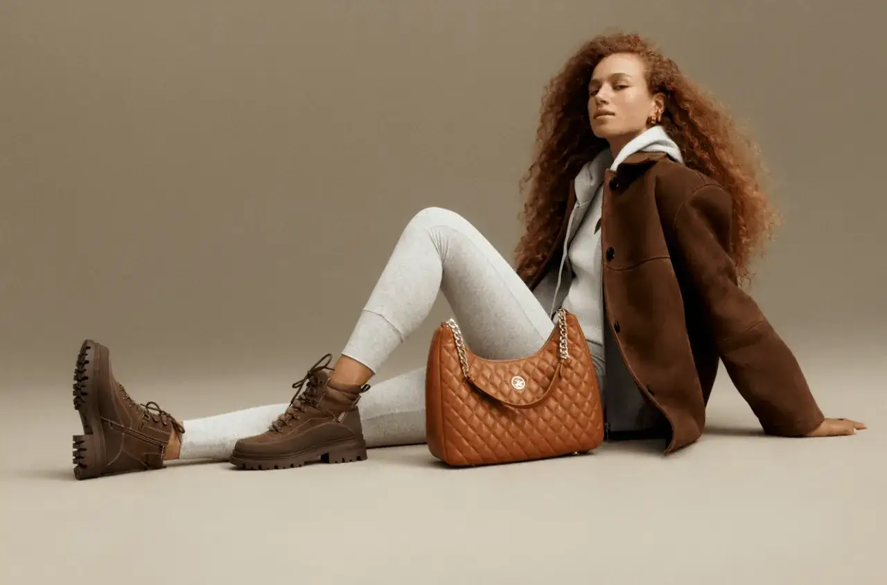 Kobieta w brązowej kurtce i szarych legginsach prezentuje torebkę Beverly Hills Polo Club, inspirowaną stylem Ralph Lauren.