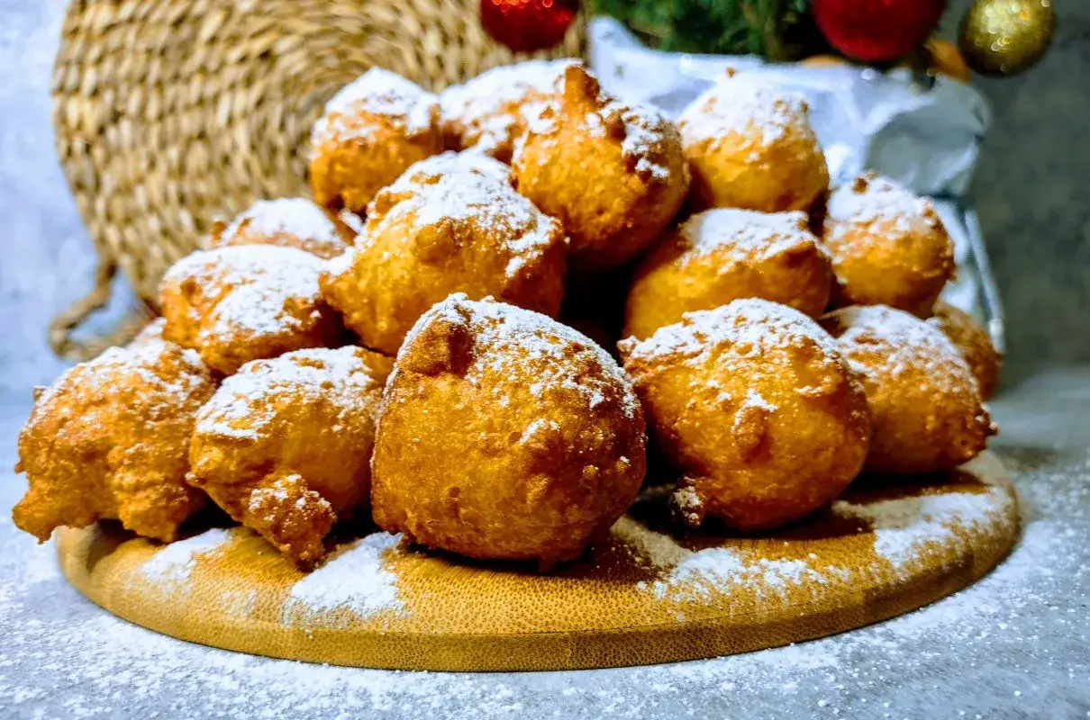 Puszyste pączki z serków homo, posypane cukrem pudrem, wyglądają jak śnieżne kule na drewnianej desce.