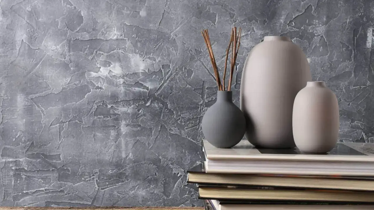 Szare wazony i patyczki na książkach na tle strukturalnego tynku. Dowiedz się, czy tynk dekoracyjny można malować.