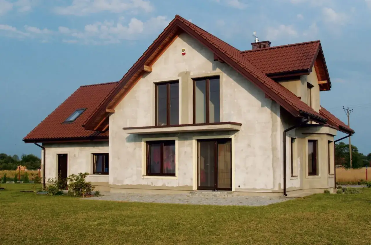 Dom w budowie z brązowym dachem, w tle linia wysokiego napięcia.